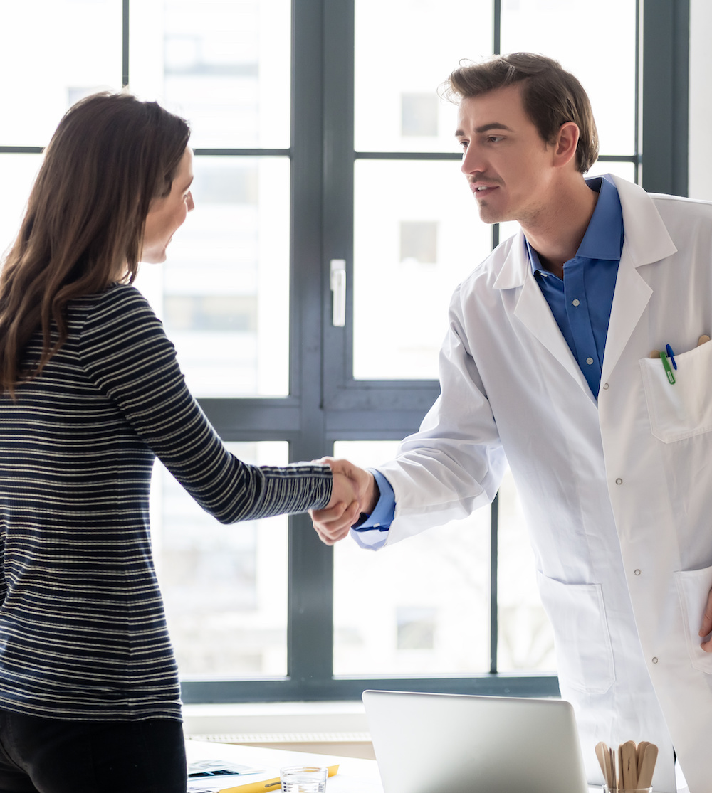 Reliable physician and female patient shaking hands before consultation